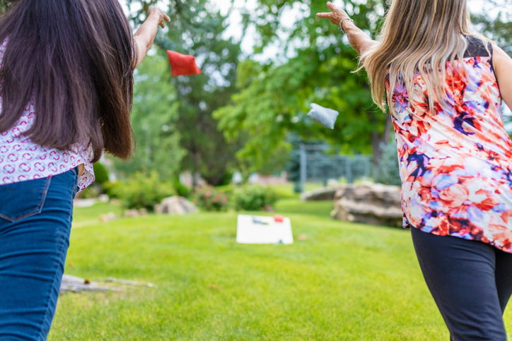 In Western Colorado Two Adult Senior Female Friends in focus in foreground with backs to camera Having Fun Together Outdoors Playing Bean Bag Toss Corn Hole Game in lush green setting with bean bag and game board blurred in background Part of Two Adult Senior Female Friends Having Fun Together Outdoors Series 4K Video Also Available for this Photo Series (Shot with Canon 5DS 50.6mp photos professionally retouched - Lightroom / Photoshop - original size 5792 x 8688 downsampled as needed for clarity and select focus used for dramatic effect)